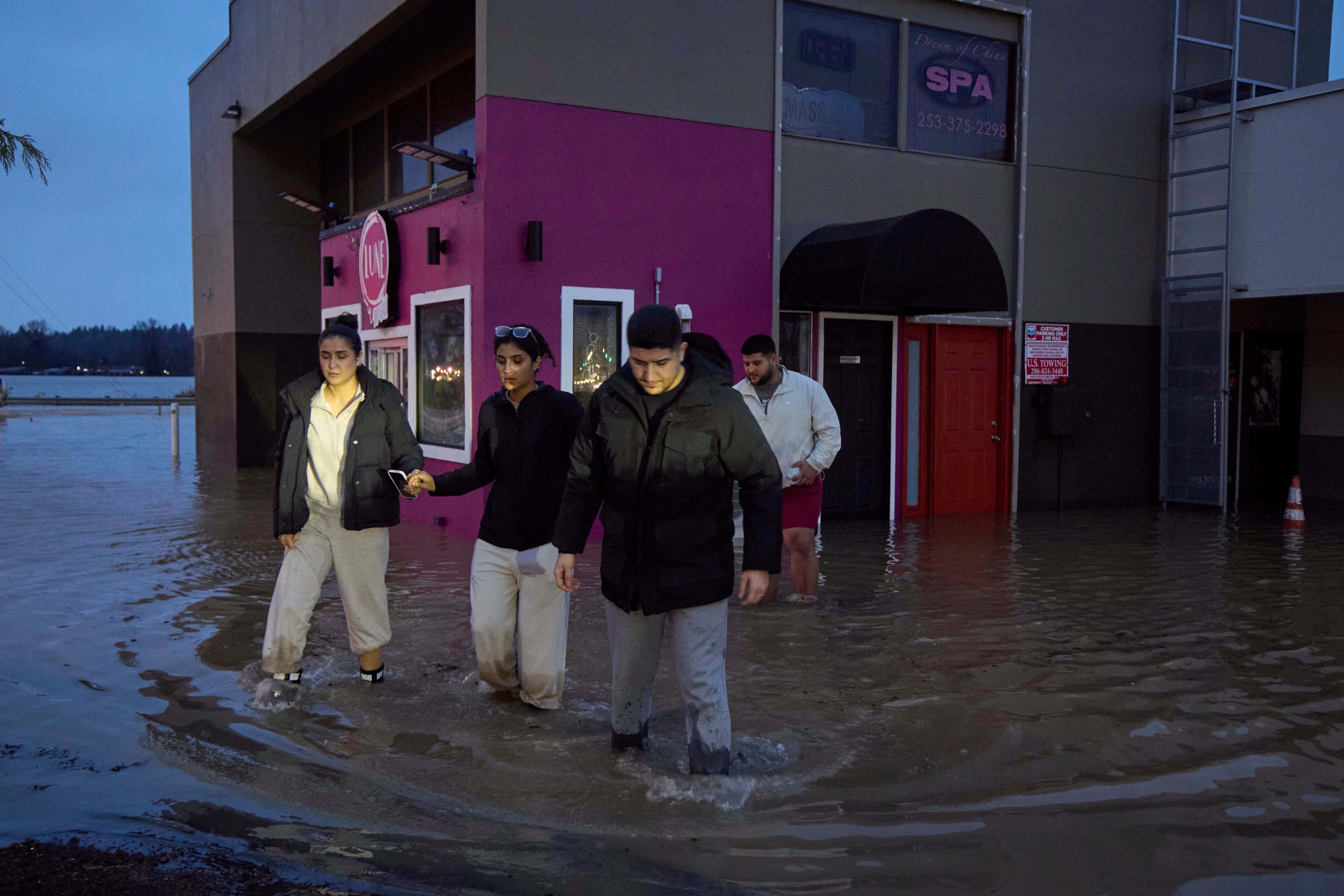 Owners of a deli business Karrar Hesham, far right, and sister Zahrha Hesham, far left, along with Hanadi Hesham, center, and Yousif Hesham, back, walk through the flood waters after checking on the state of their store, Wednesday, Dec. 10, 2025, in Auburn, Wash.