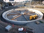 In this provided photo, the pit for the historic locomotive turntable at Oregon Rail Heritage Center is installed. A yellow construction machine sits in a large round pit, with wooden supports installed throughout the pit.