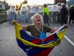 Consuelo Marquez holds a Venezuelan flag in front of police blocking demonstrations against the official election results declaring President Nicolas Maduro's reelection, the day after the vote in Caracas, Venezuela, Monday, July 29, 2024. 