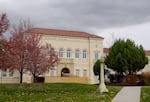 A two-story historic office building with a beige facade and a red tiled roof. Wood barriers are erected in front of Inlow Hall as the building is being renovated.