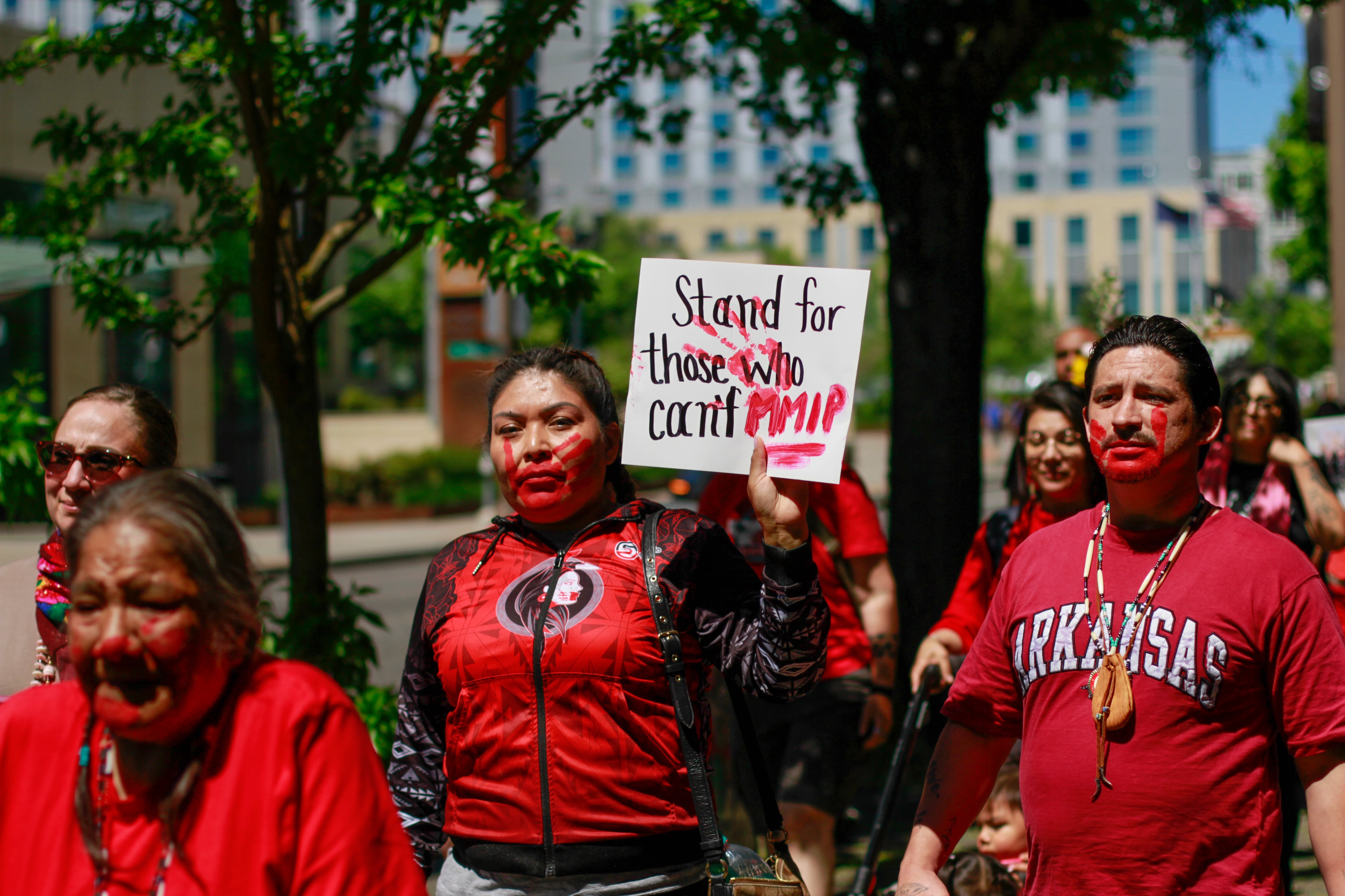 Dozens of people wearing red shirts, ribbon skirts and red handprints painted over their mouths walked the three quarters of a mile to the Willamette River at Duckworth Memorial Dock, where they took part in a ceremony, joined from the water by the 7 Waters Canoe Family. People held signs with phrases like “Stand for those who can’t,” “We are their voices,” “Honor their spirit” and more.