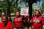 Dozens of people wearing red shirts, ribbon skirts and red handprints painted over their mouths walked the three quarters of a mile to the Willamette River at Duckworth Memorial Dock, where they took part in a ceremony, joined from the water by the 7 Waters Canoe Family. People held signs with phrases like “Stand for those who can’t,” “We are their voices,” “Honor their spirit” and more.