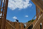 A worker building the roof stands atop the wood frame of a home under construction.