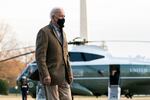 Biden, in a jacket and tie and wearing a facemask walks with Marine One in the background. A U.S. Marine, in full uniform, stands at attention near the front of the chopper.