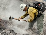A firefighter uses a hoe hand tool to extinguish smoke billowing from the ground.
