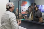 Julien Simonis, Programme Manager for Cacao of Excellence, explains the physical quality evaluation of cocoa beans to visitors through a glass partition at the Chocolate Museum. Simonis demonstrates the sensory and visual analysis process, which involves inspecting halved beans to verify fermentation levels and aromatic potential.