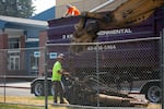 (From left) Steve Crowe unchains a piece of heavy equipment while Mitch Stills looks on in Bend, Ore., on July 22, 2024. 3 Kings Environmental will managing the demolition and removal of asbestos contaminated materials found in the Bend Senior High School auditorium.
