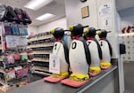 A line of fake penguins sitting on a counter. Behind them are rows of skates and soakers