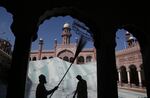 Two people work with cleaning tools while the minaret of a mosque rises in the background behind them.
