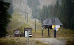 An inert ski lift hangs on cables that lead up a grassy mountainside.