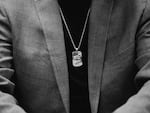 This black-and-white photo shows Aiden Jugueta's necklace, which has a dog tag pendant with an eagle and American flag on it. Aiden is wearing a dark shirt and a blazer on top of it.