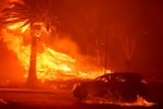 A car drives past flames from the Franklin Fire at Pepperdine University in Malibu, Calif., Tuesday, Dec. 10, 2024.