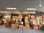 Pictured are 9 rows of moving boxes, each filled with various goods mean to be shipped to Hawaii. The boxes vary in size, but are all brown, many with the distinct orange Home-Depot logo. They tower up to the ceiling.