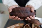 A technician holds a whole, dried cocoa pod at the Cacao of Excellence laboratory. According to the initiative's quality standards, proper drying is vital, as it reduces moisture from 60% to approximately 7% to prevent mold and develop flavor precursors. Led by the Alliance of Bioversity International and CIAT, the lab analyzes samples from over 50 origins to recognize superior cocoa quality.