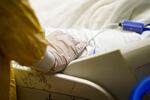 A gloved hand holds the hand of a COVID-19 patient who is in a hospital bed.