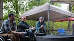 Three people sit together at a park picnic area. At least two of them are seated in wheelchairs.