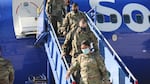 People wearing military camouflage exit an airplane while wearing face coverings.