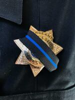 A close up image of a police badge, partially covered in a black ribbon with a blue stripe down the middle.