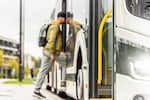 A man wearing a backpack boards a bus.