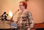 A person with red hair and glasses speaks at a podium.