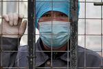 A worker wearing a mask, watches from inside a hospital across the Wuhan Center for Disease Control and Prevention after the World Health Organization team arrive to make a field visit in Wuhan in central China's Hubei province on Monday, Feb. 1, 2021.