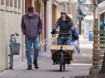 Ben Hodgson, left, walks along as Diana Rempe rides the Street Books library bike in downtown Portland, traveling to another library site in February. Earlier in the pandemic, the library shifted to more one-on-one outreach in an attempt to avoid the type of in-person gathering created by a typical bike library shift, though those have resumed. 