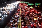 Multiple lanes of cars and other vehicles crawl slowly in rush-hour traffic on Interstate 405 in Los Angeles in March 2022. The scene is after dark, and the vehicles have their headlights and taillights turned on.