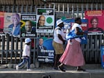 Women with children walk past election posters in Tembisa, east of Johannesburg, South Africa 2024.