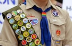 FILE - Merit badges and a rainbow-colored neckerchief slider are affixed on a Boy Scout uniform. The U.S. organization, which now welcomes girls into the program and allows them to work toward the coveted Eagle Scout rank, announced May 7, 2024, that it would change its name to Scouting America as it focuses on inclusion.