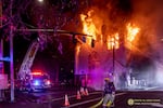 A firefighter looks over their shoulder at a fire burning the top of the former Portland Korean Church. It is night time.