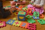 Children play with colorful, numbered puzzle pieces on the floor. Their faces are not visible.