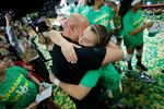 A woman in green jersey embraces a man in black shirt, with other women in green jerseys surrounding them.