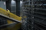 This photo shows the automated storage and retrieval system in DigiKey’s product distribution center, which is four stories high. The space has tall, long rows of metal shelves. A worker walks up a staircase with yellow handrails.