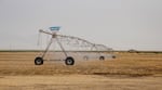 A long row of irrigation equipment sprays water on some soil.