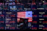 In this March 16, 2020 file photo, a United States flag is reflected in the window of the Nasdaq studio, which displays indices and stocks down, in Times Square, New York.