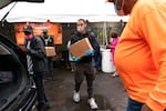 A Black man serving as a volunteer takes a box of food to put in a car's trunk.