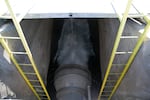 A view from above showing a large pipe with water flowing out and two yellow ladders leading down to it.