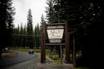 A large wooden sign advertises Anthony Lakes as a car drives by on a windy forest road.