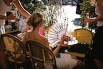 A young woman sitting on a terrace shields herself from the sun with a fan decorated with Parisian landmarks during a severe heat wave in Paris on Aug. 12, 2026.