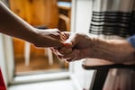 A closeup photo of two hands demonstrates an older man clasping the hand of a person who is offering a helping hand.