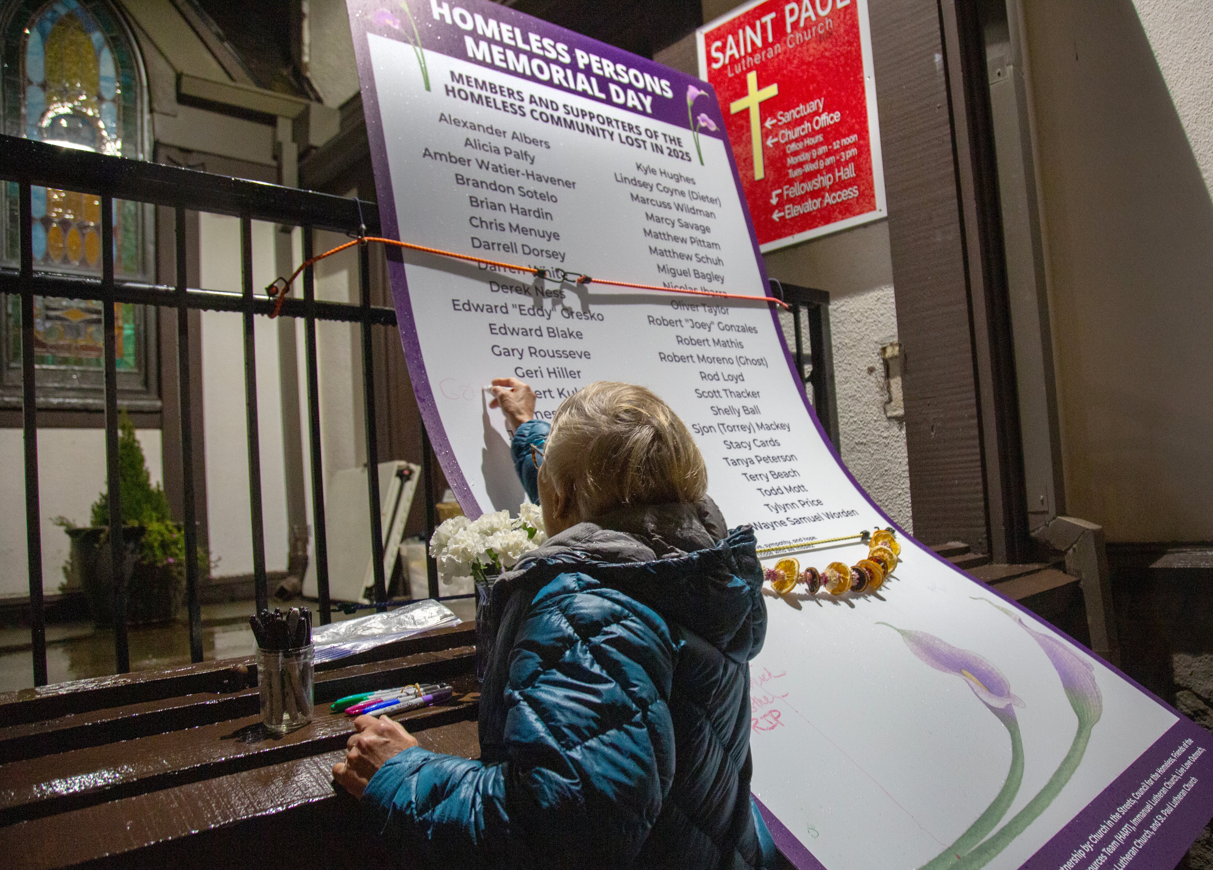 St. Paul Lutheran Chuch Pastor Linda Marousek writes a note on a list of people who died in 2025 at the Vancouver homeless persons memorial on Dec. 21, 2025.