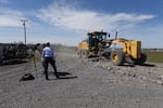 Kotek stands with her back to the camera as a piece of heavy equipment spits up gravel as it goes by.