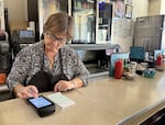 Owner Karen Carlton works on a point-of-sale machine with a customer's check over the counter at Joe Brown's Cafe in Vancouver, Wash., on Sept. 27, 2026.