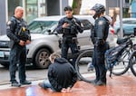 (Left to right) Sgt. Jerry Cioeta, and Officers Donny Mathew and Joey Yoo, await transport for a man arrested on a fentanyl-related charge, Feb. 7, 2024. The work was part of a pilot program between Portland Police Bureau’s Central Bike Squad and addiction recovery providers, launched in December, 2023, which has now been funded as part of the coordinated fentanyl emergency response between the state, city of Portland and Multnomah County.