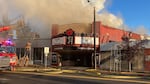 A theater covered in smoke while firefighters climb a ladder onto a nearby roof.