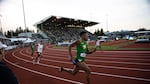 Oregon sprinter Orwin Emilien carries the baton in the 4x400-meter relay. Historic Hayward Field's West Grandstand looms in the background.