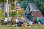 A man sits outside his camp this September in Southwest Portland. With an unexpected budget surplus, the city council has committed $18.8 million to homeless services as part of a city-county agreement on homelessness.