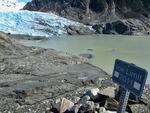 A sign juts from rocks with the words "Ice Limit 2011." The icy edge of a glacier can be seen at a distance away from the sign.