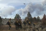 A ground crew of firefighters walk to the fire line of the Falls Fire, located northwest of Burns, Oregon, on Wednesday, July 17, 2024. Overhead, a helicopter flies above the fire.