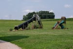 Playground tube slides stand on Brian Smyser’s Farm in a grassy area. One tube slide has a twist in it.